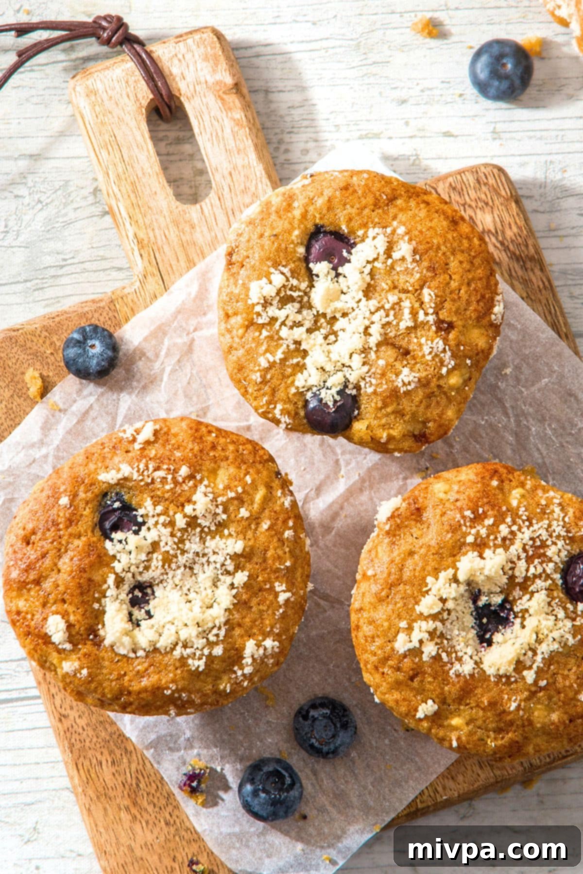 Cottage Cheese Blueberry Muffin Recipe(Gluten-Free) Three perfectly baked cottage cheese and blueberry muffins presented on a parchment-lined wooden board.