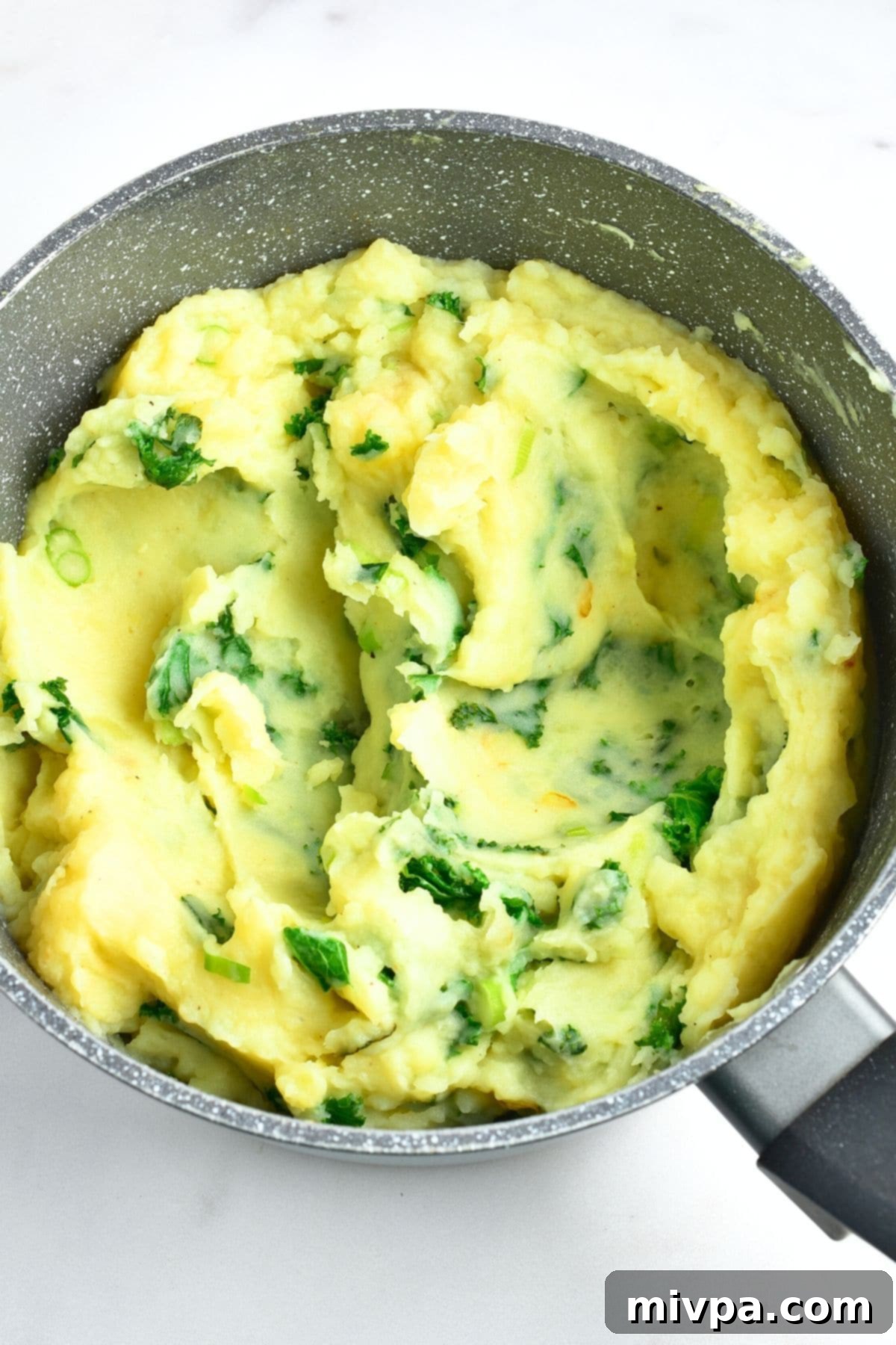 Seasoning Irish Mashed Potatoes with Kale Kale mixed into mashed potatoes in a pot, ready for final seasoning