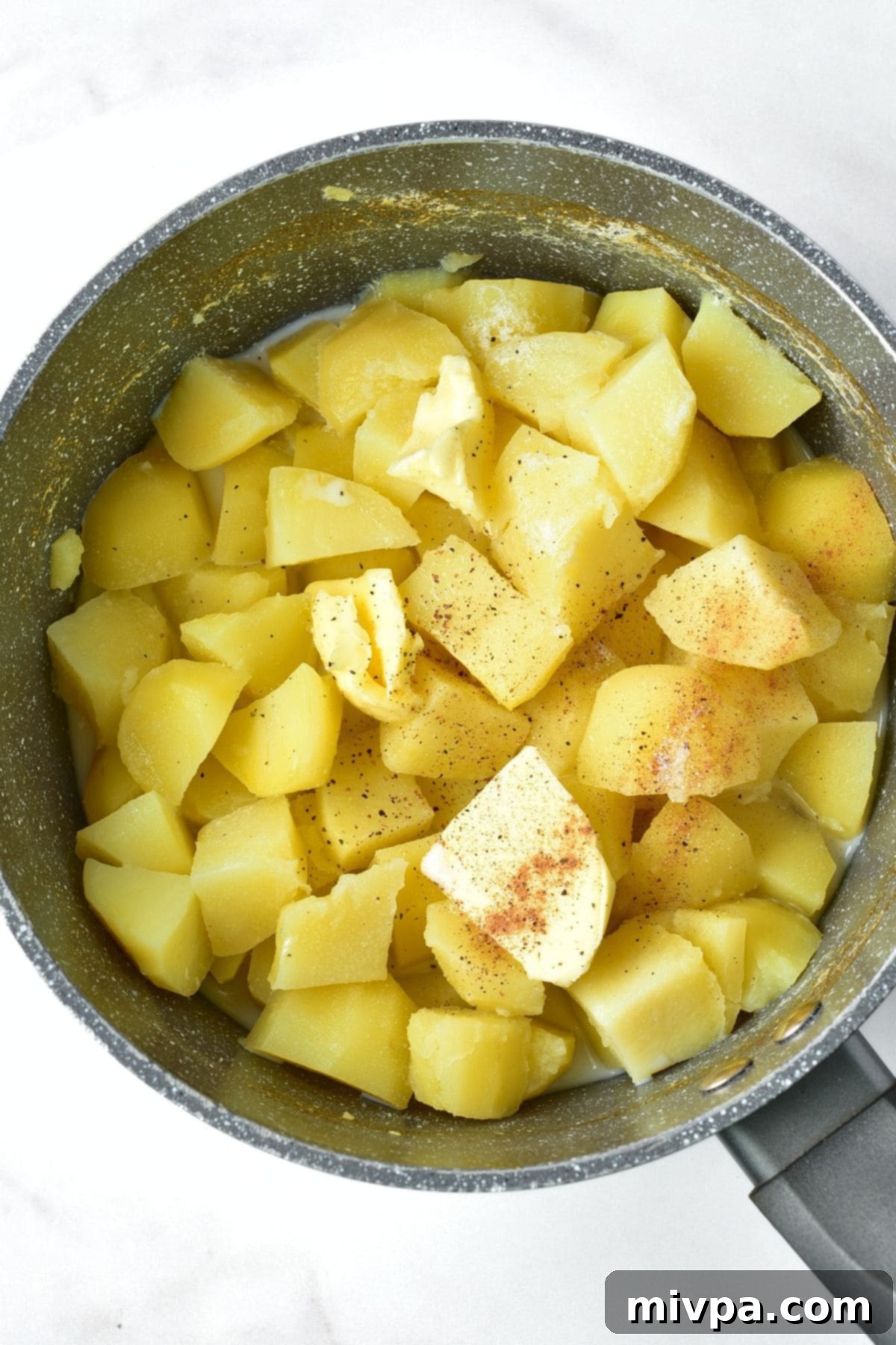 Mashing Irish Mashed Potatoes A pot of cooked cubed potatoes with milk, butter, and nutmeg ready for mashing