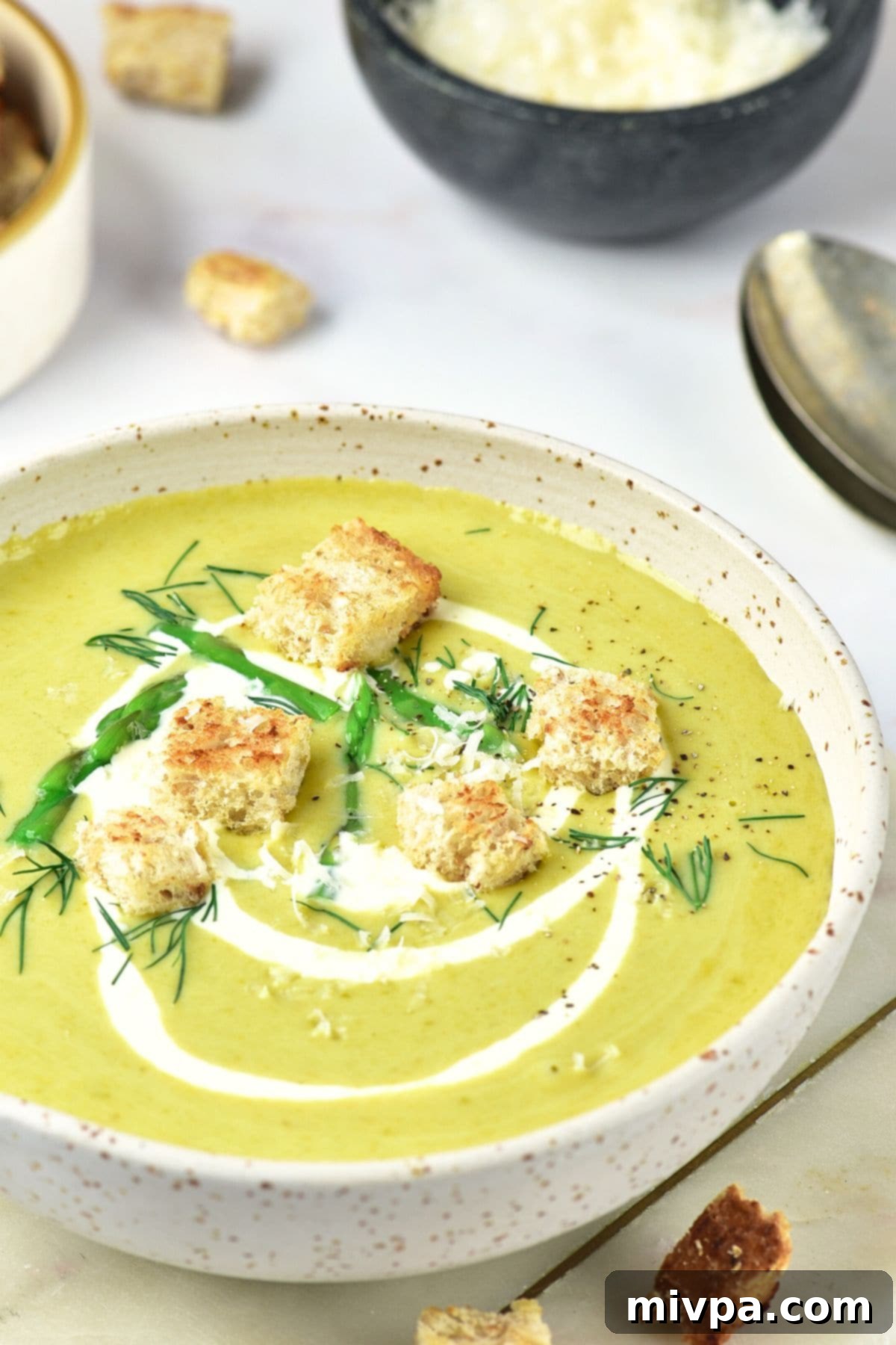 Up close view of a bowl of asparagus potato soup topped with croutons.