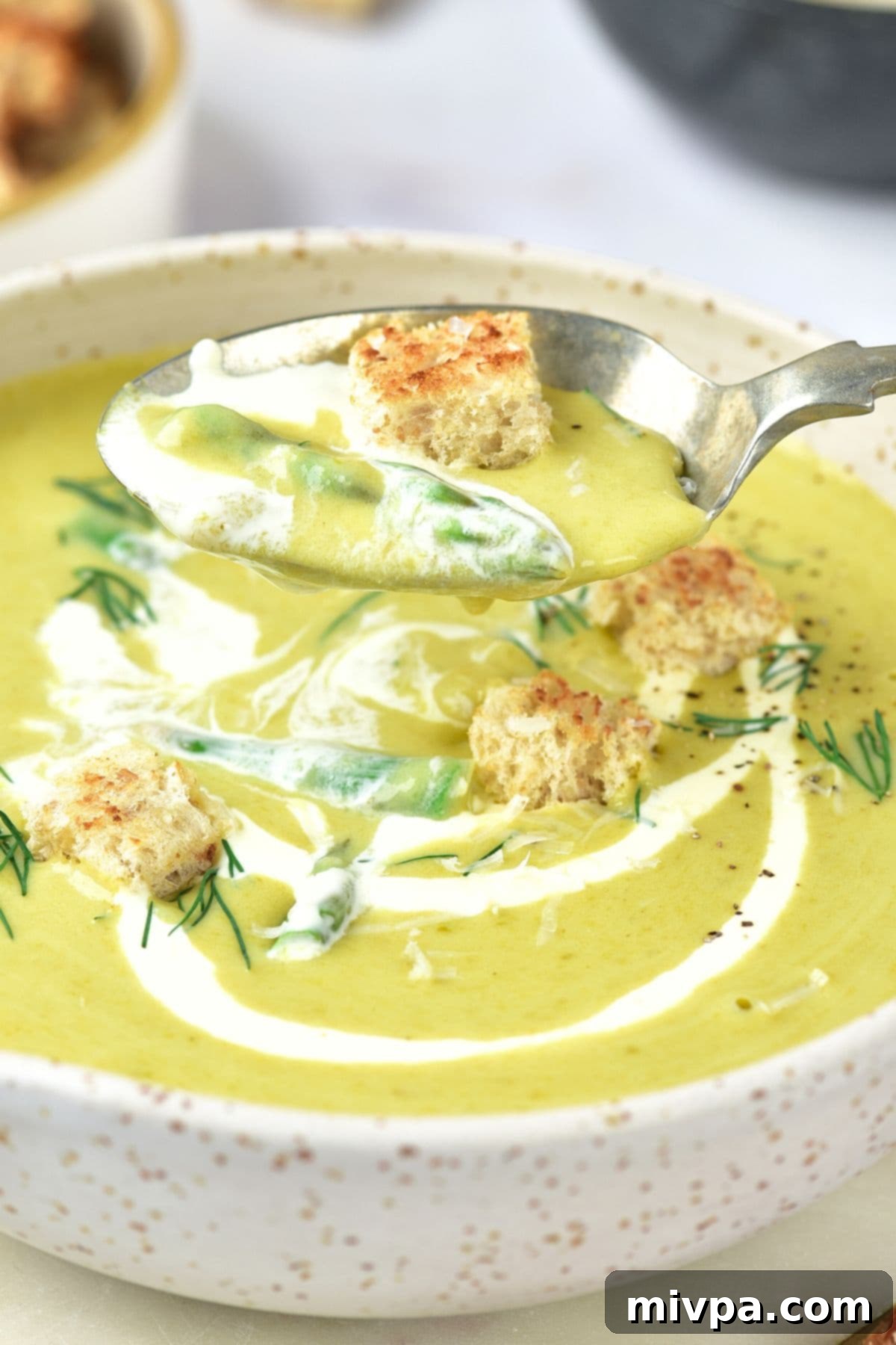 Holding up a spoonful of asparagus and potato soup from a bowl.