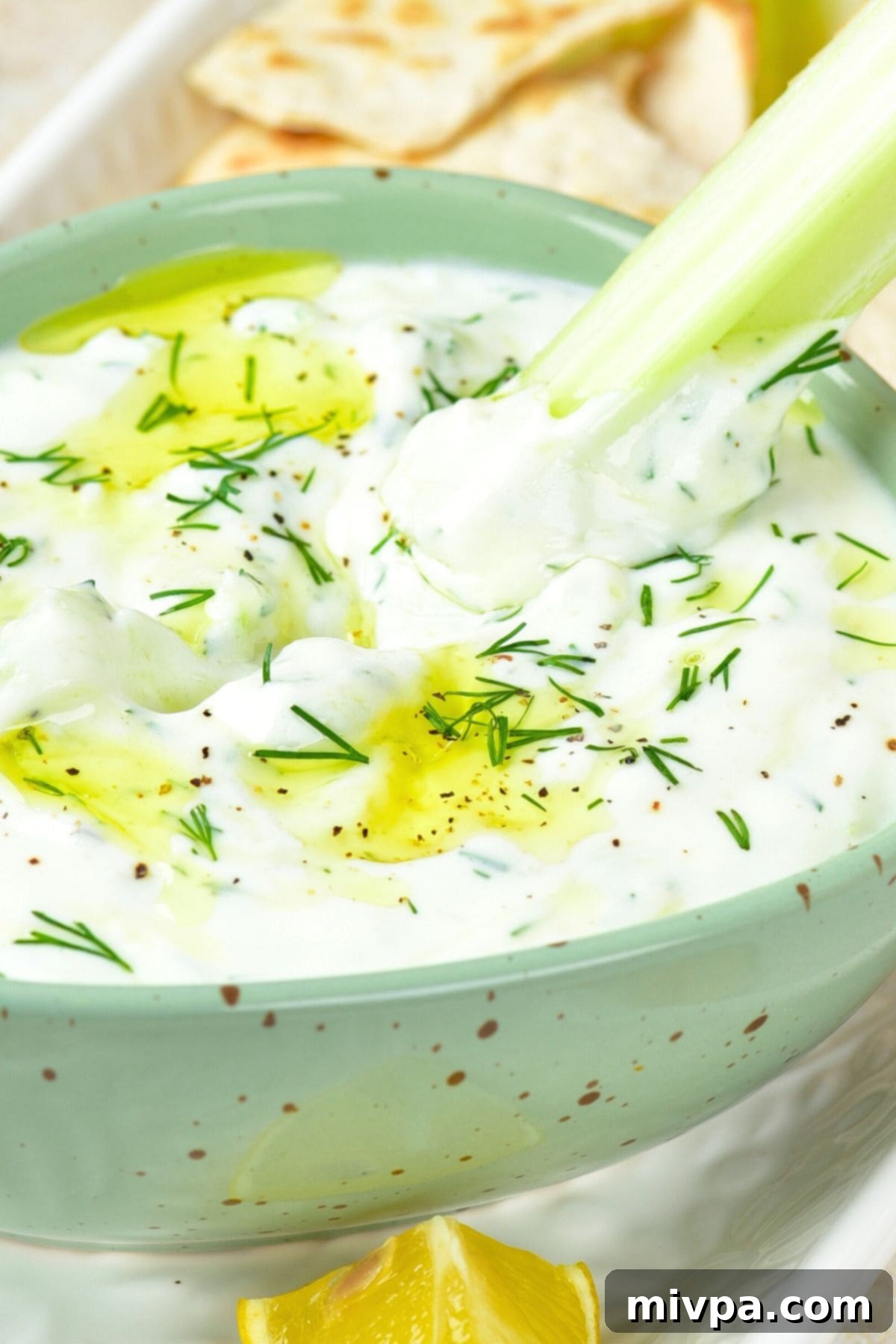 Dipping a celery stick into a bowl of dairy-free tzatziki dip, showcasing its creamy texture.