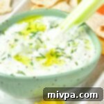 Dipping celery stick into a bowl of dairy-free tzatziki, a refreshing and creamy vegan dip.