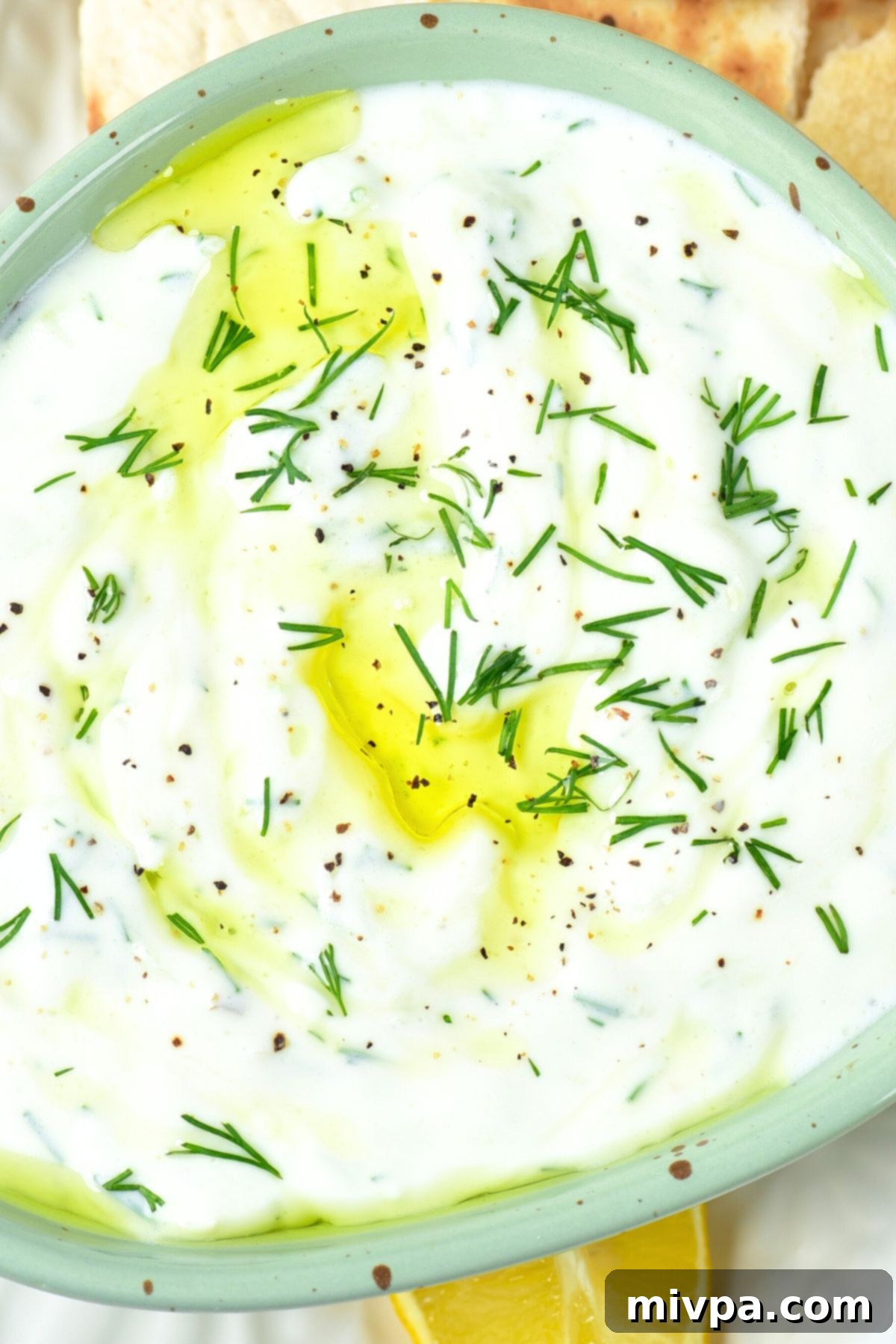 Top down view of a bowl of dairy-free tzatziki sauce sprinkled with fresh dill, ready to be served.