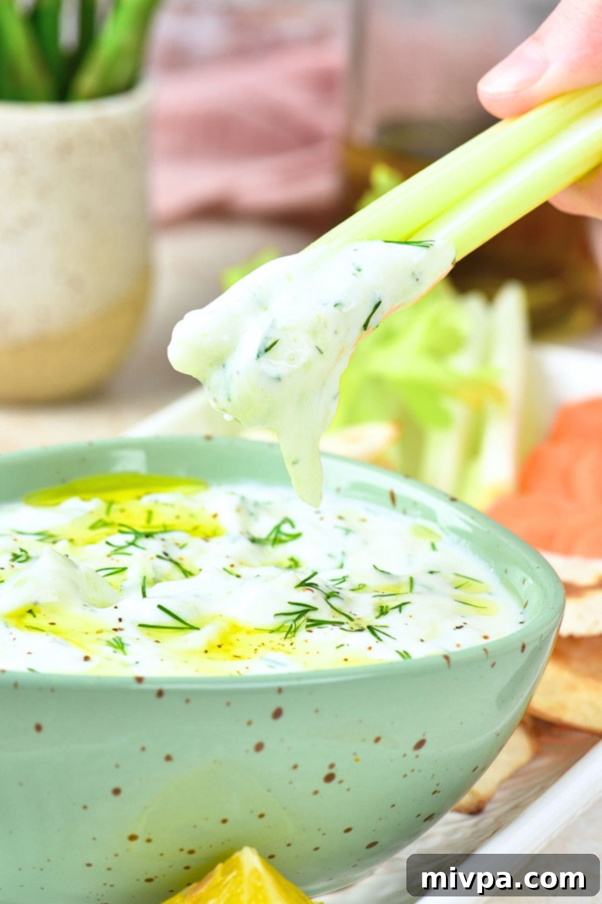 Dipping a celery stick into a bowl of tzatziki sauce (dairy-free, gluten-free), highlighting its refreshing quality.