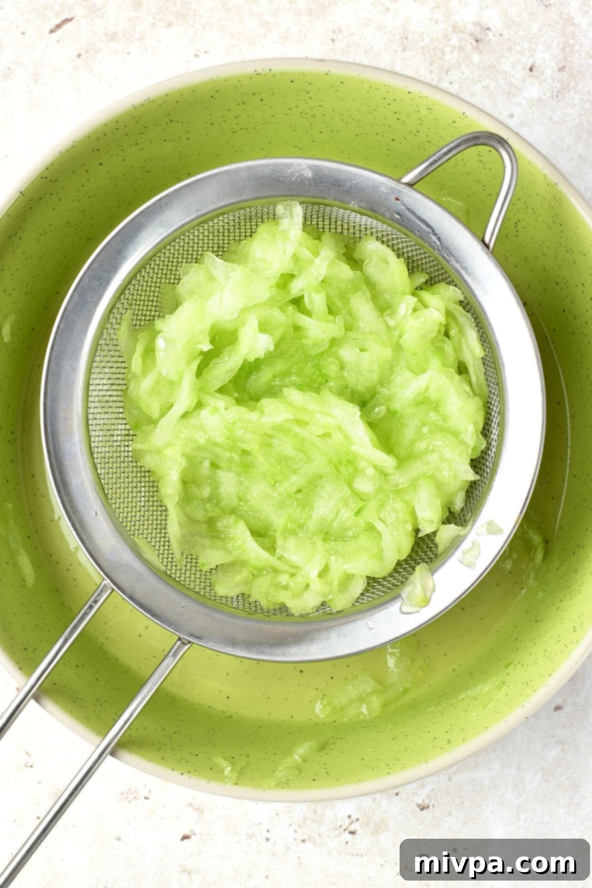 Squeezing out moisture from grated cucumber using a sieve, demonstrating the crucial draining step.
