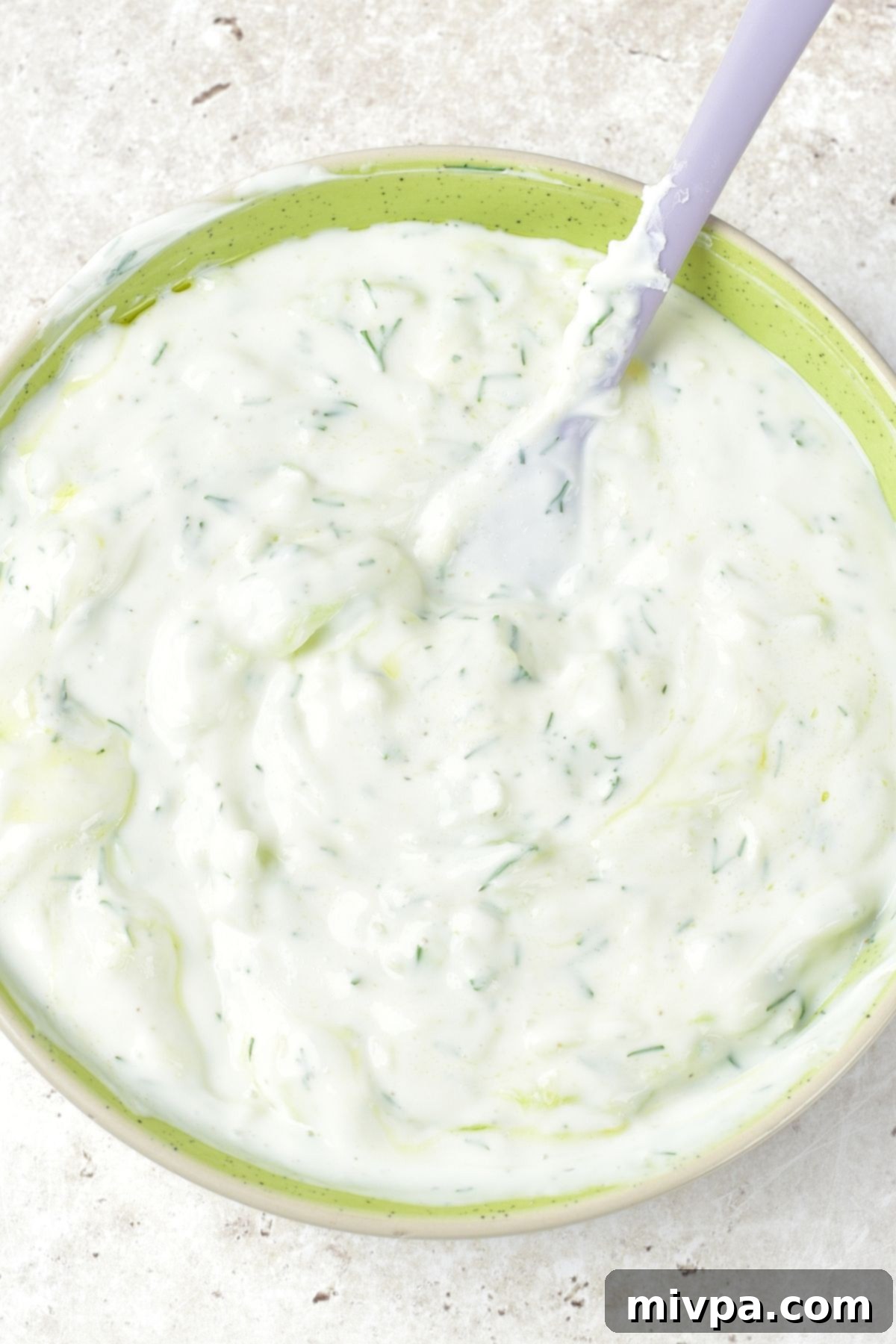 A spoon in a bowl of perfectly mixed non-dairy tzatziki, showing its smooth consistency.