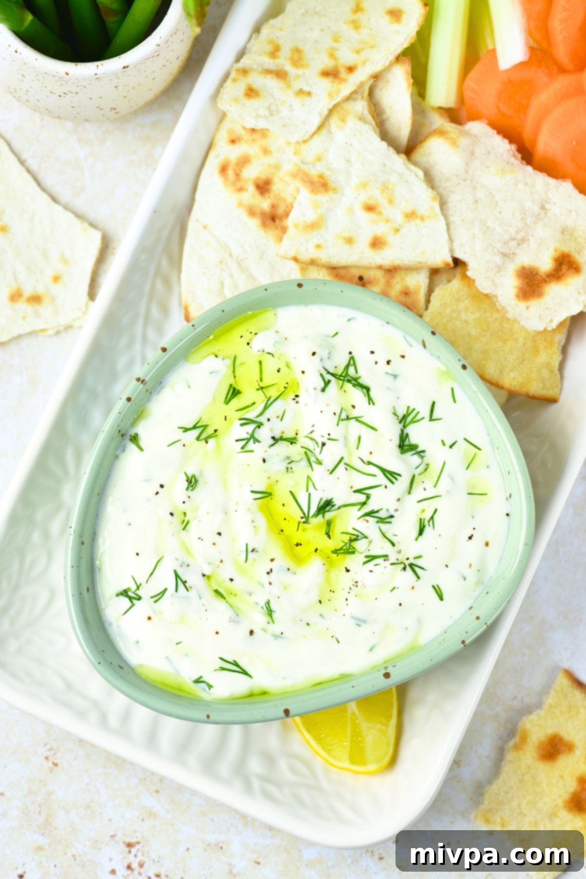 Top down view of a bowl of dill tzatziki with various crackers and fresh dill garnish.
