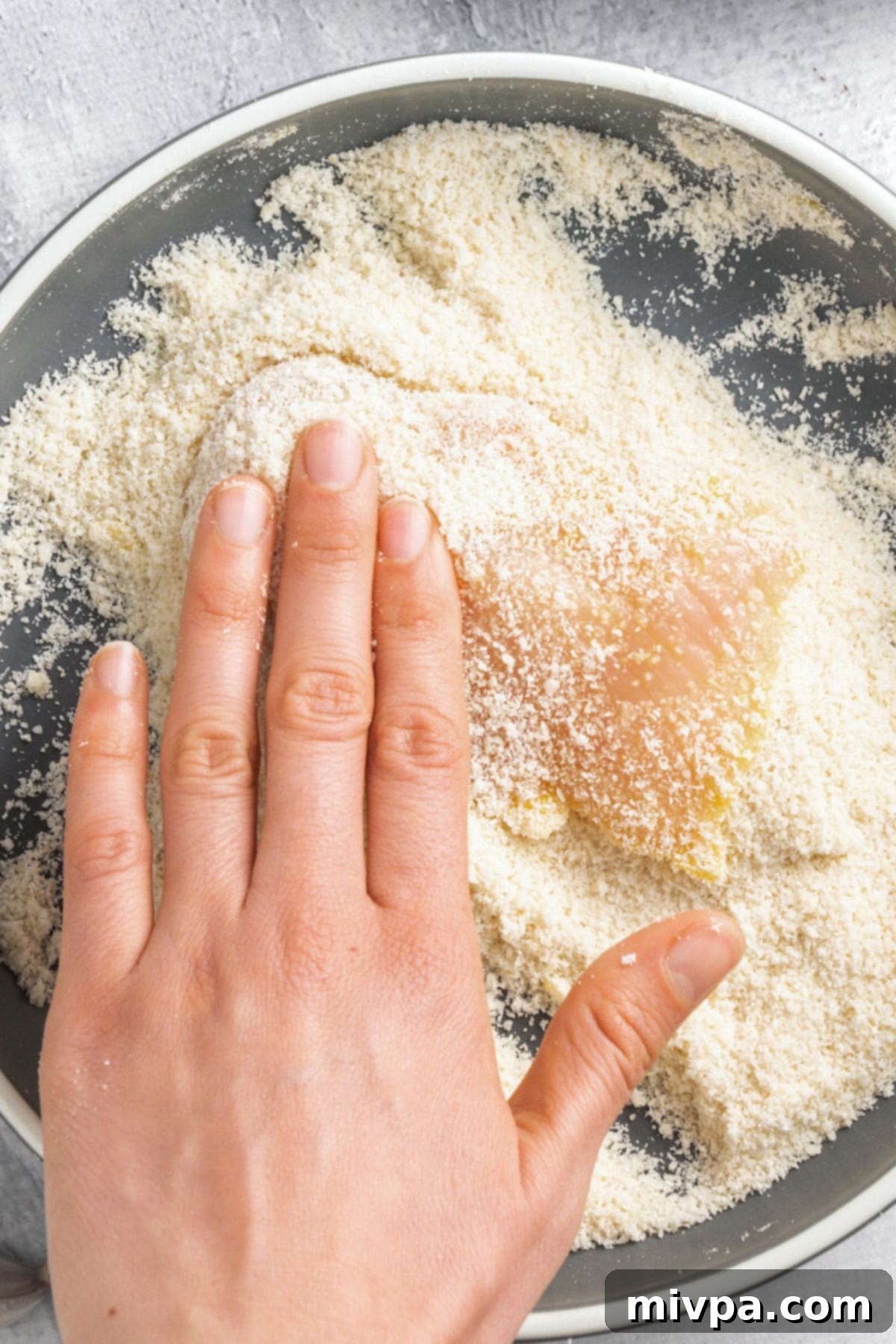 A chicken fillet being coated thoroughly in a shallow bowl of gluten-free breadcrumb mixture, ensuring an even and complete coverage.
