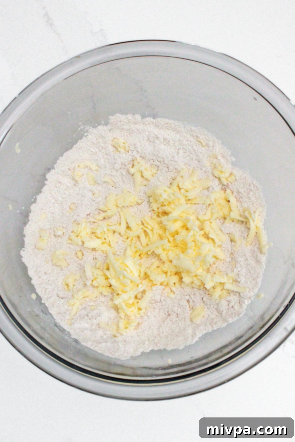 How to Make Ritz Crackers (Gluten-Free) Grated butter on top of flour mixture in glass bowl
