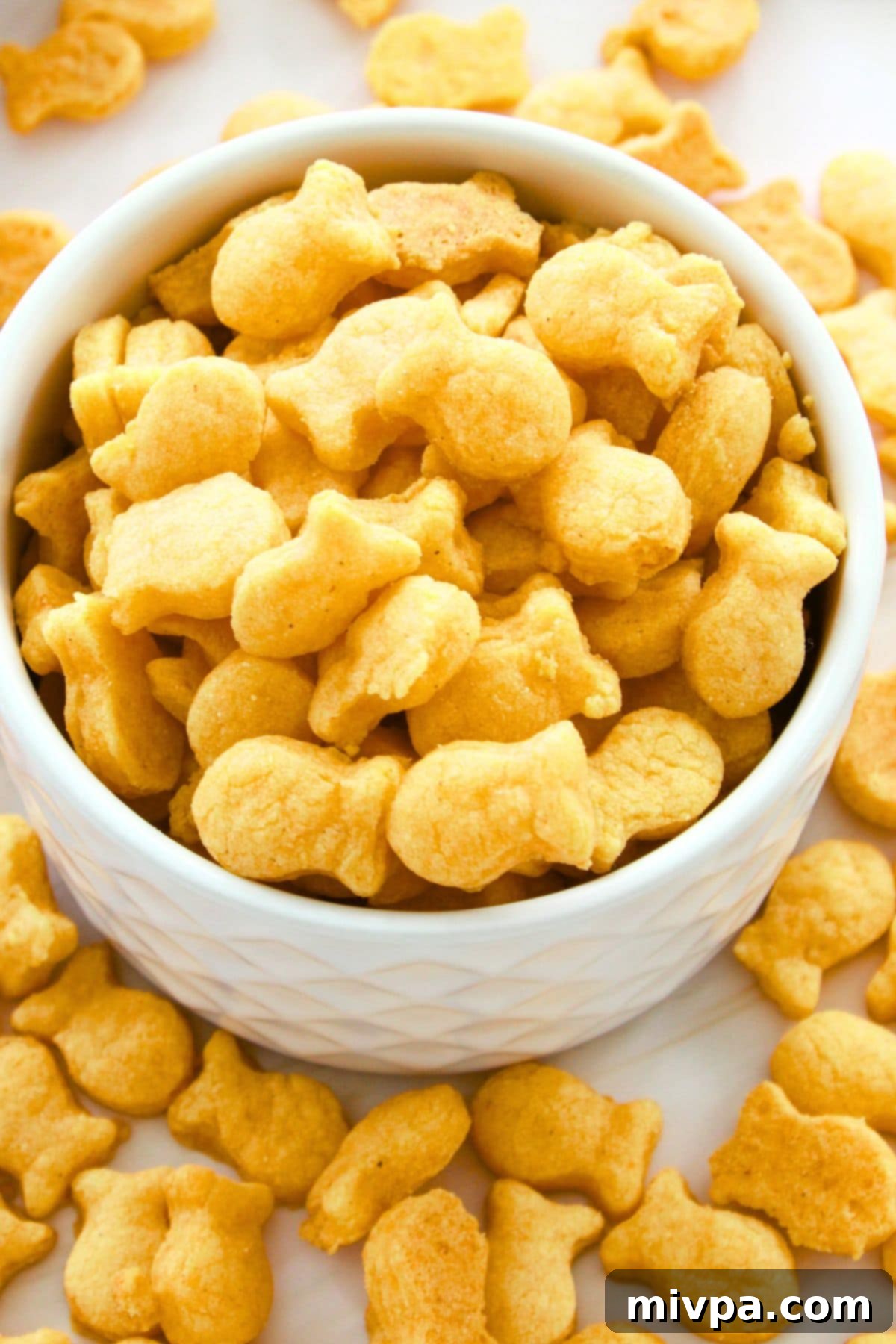 Gluten-Free Goldfish Crackers (Dairy-Free Option) Top down view of a vibrant bowl filled with golden-brown homemade gluten-free goldfish crackers, invitingly ready for snacking.