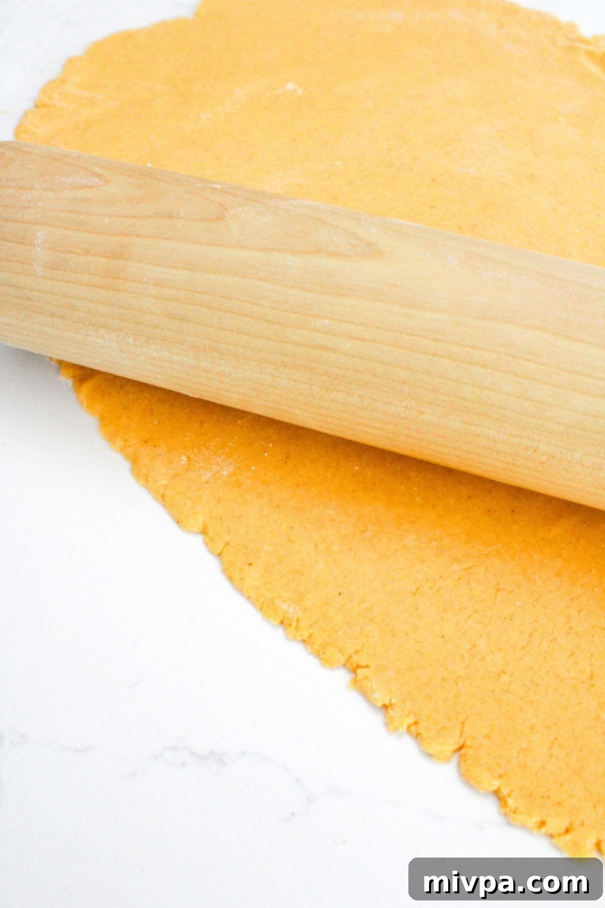 Copycat Gluten-Free Goldfish A rolling pin carefully rolling out the vibrant orange cracker dough on a lightly floured surface, aiming for an even thickness.