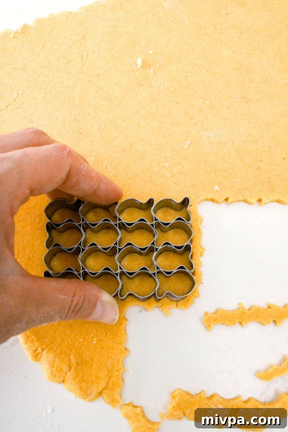 Gluten-Free Goldfish Cracker (Dairy-Free Option) A small goldfish-shaped cookie cutter pressing into the rolled-out orange dough, creating individual cracker shapes.