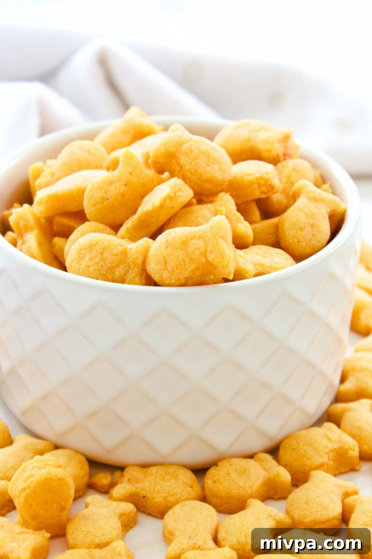How to Make Your Own Goldfish Crackers A close-up shot of a small white bowl overflowing with homemade goldfish crackers, emphasizing their texture and inviting appearance.