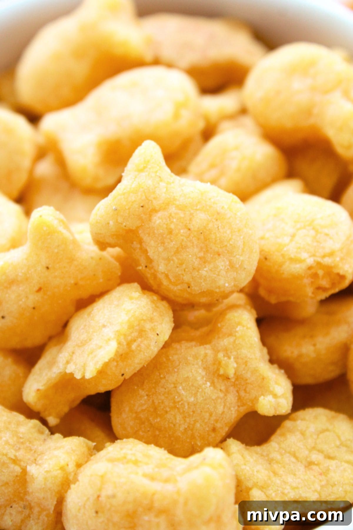 Gluten-Free Homemade Goldfish Crackers An extreme close-up of several perfectly baked, golden-brown gluten-free homemade goldfish crackers, showing their crisp texture and detail.