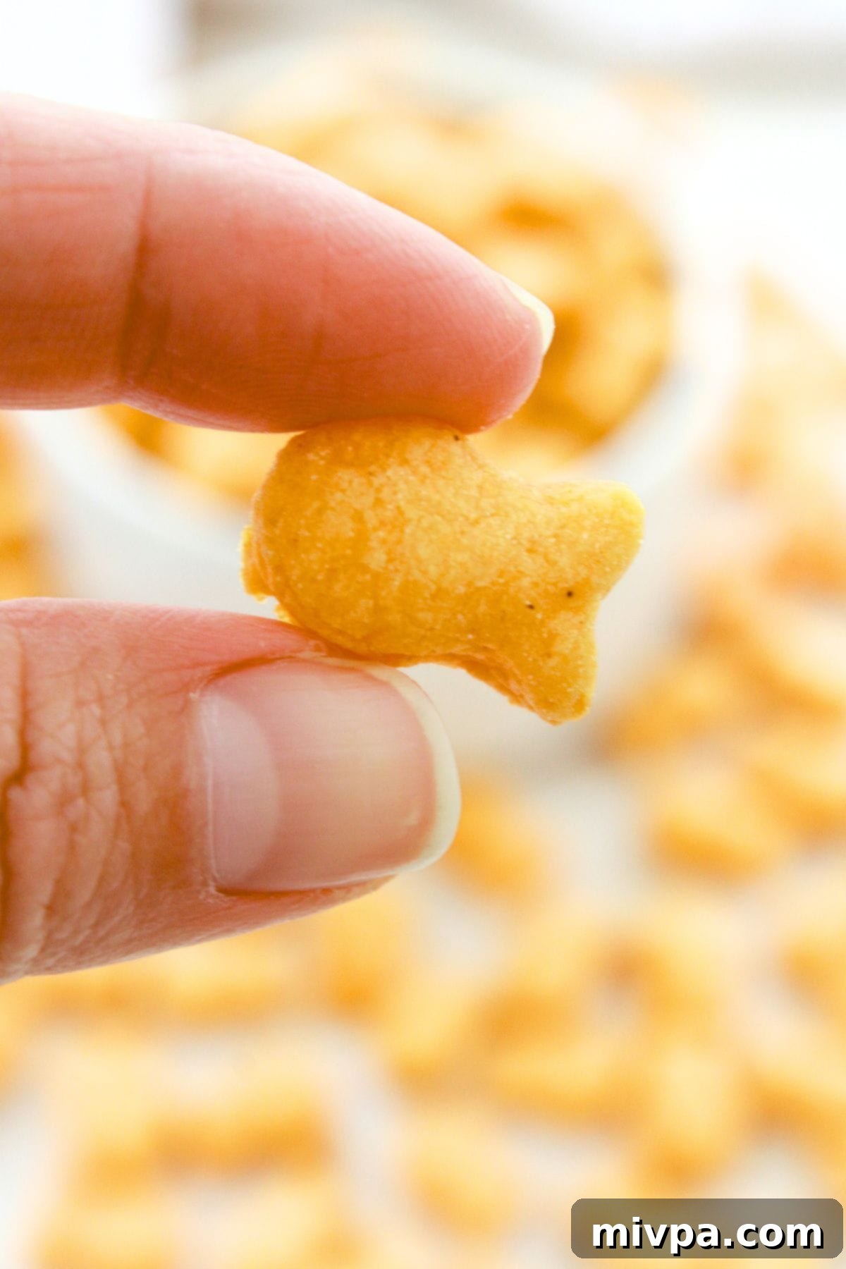 Gluten-Free Goldfish Cracker Recipe (Dairy-Free Option) A hand holding up a single small, smiling, perfectly baked gluten-free goldfish cracker against a soft-focus background.