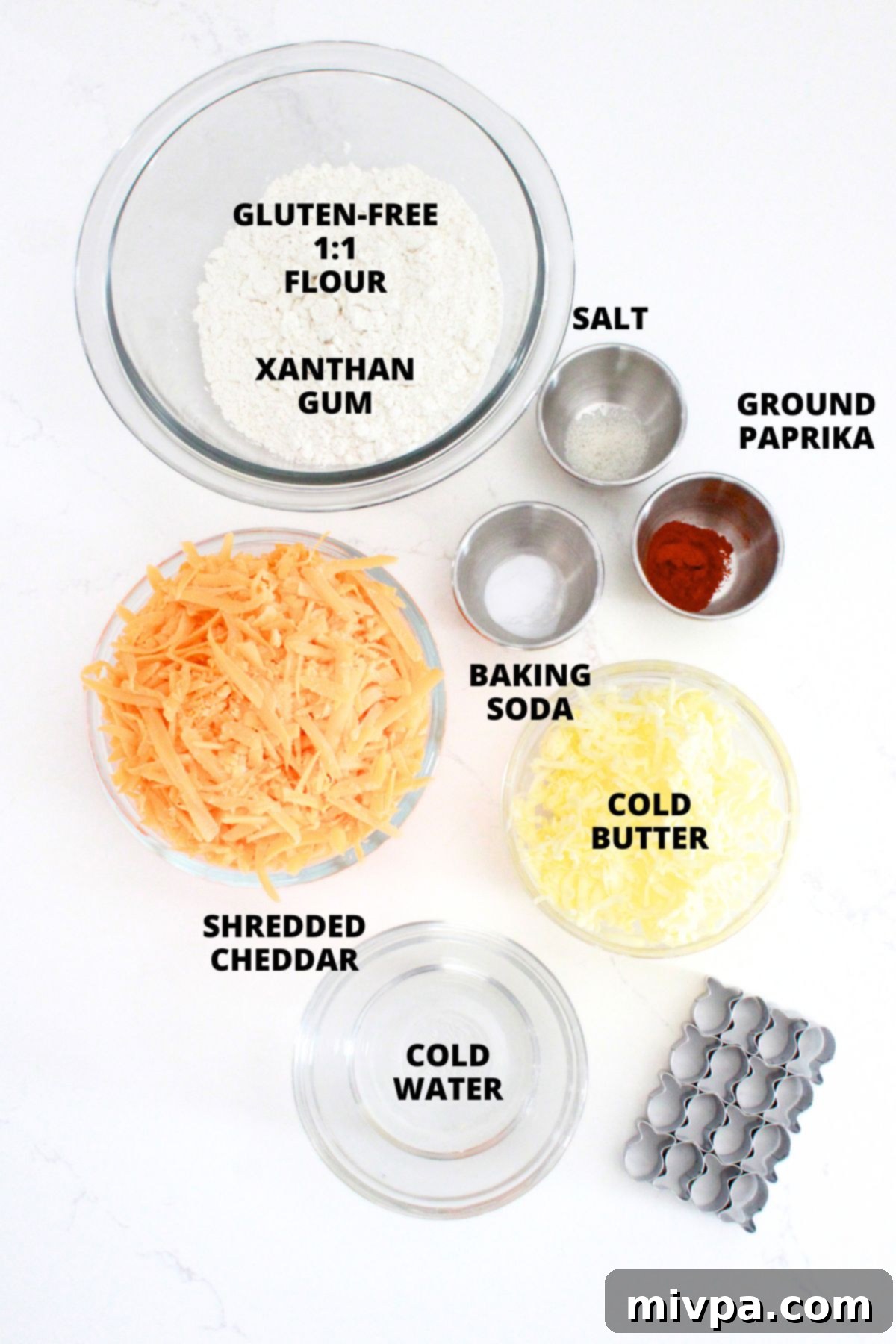 Gluten-Free Goldfish Crackers Recipe (Dairy-Free Option) A flat lay of all the fresh ingredients for gluten-free goldfish crackers recipe, including flour, cheese, butter, and spices, neatly arranged on a white board.