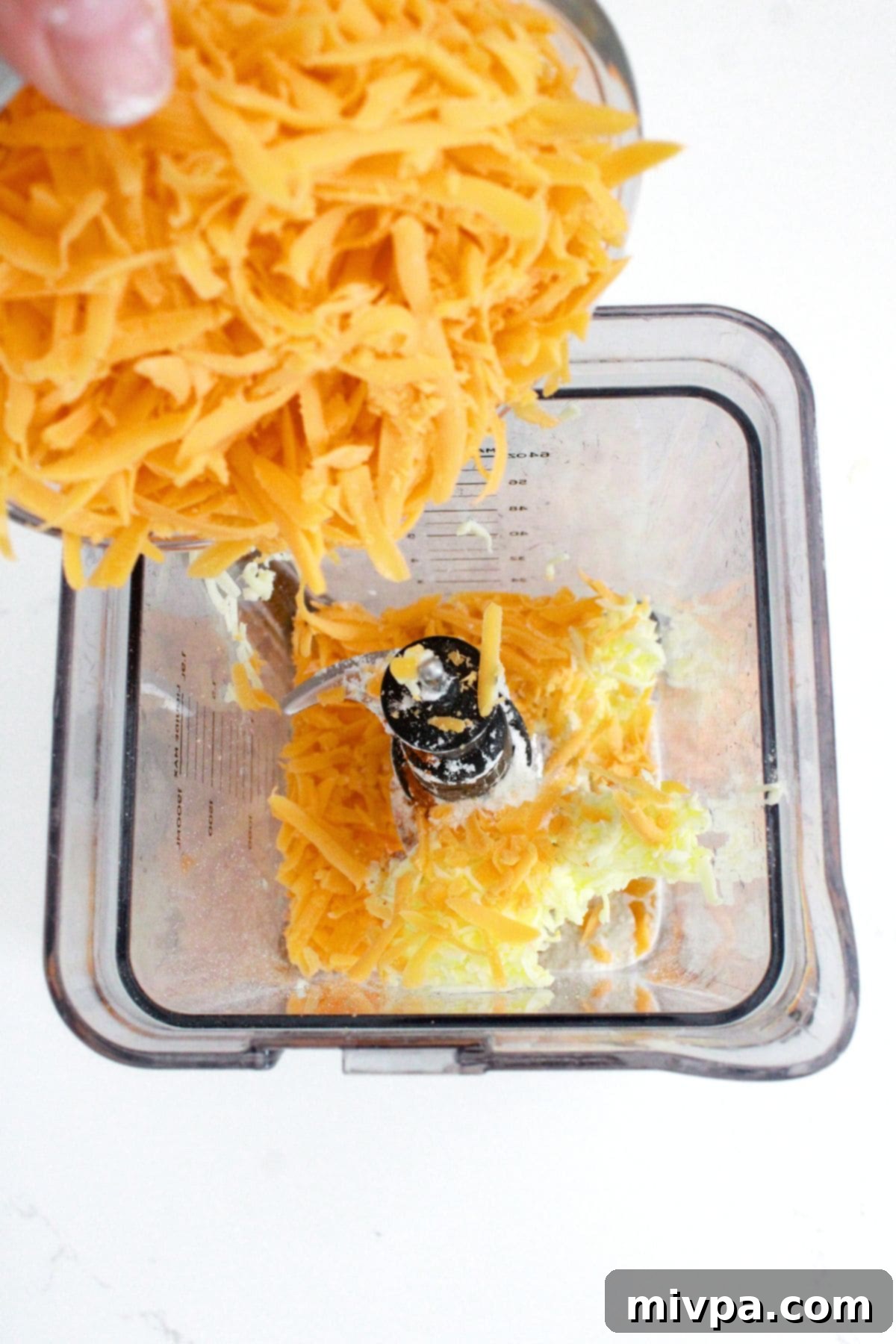 Easy Goldfish Crackers (Gluten-Free, Dairy-Free Option) Close-up of grated cold cheddar cheese being transferred into a high-speed blender, ready to be processed with other dry ingredients.