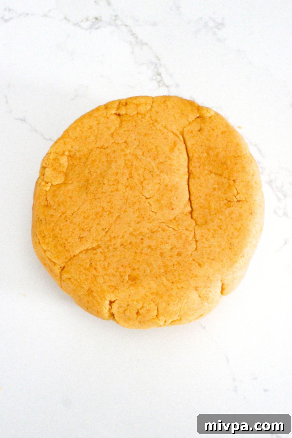 Gluten Free Copycat Goldfish Crackers The orange-yellow cracker dough, freshly formed and shaped into a smooth round disc, resting on a lightly floured work surface.
