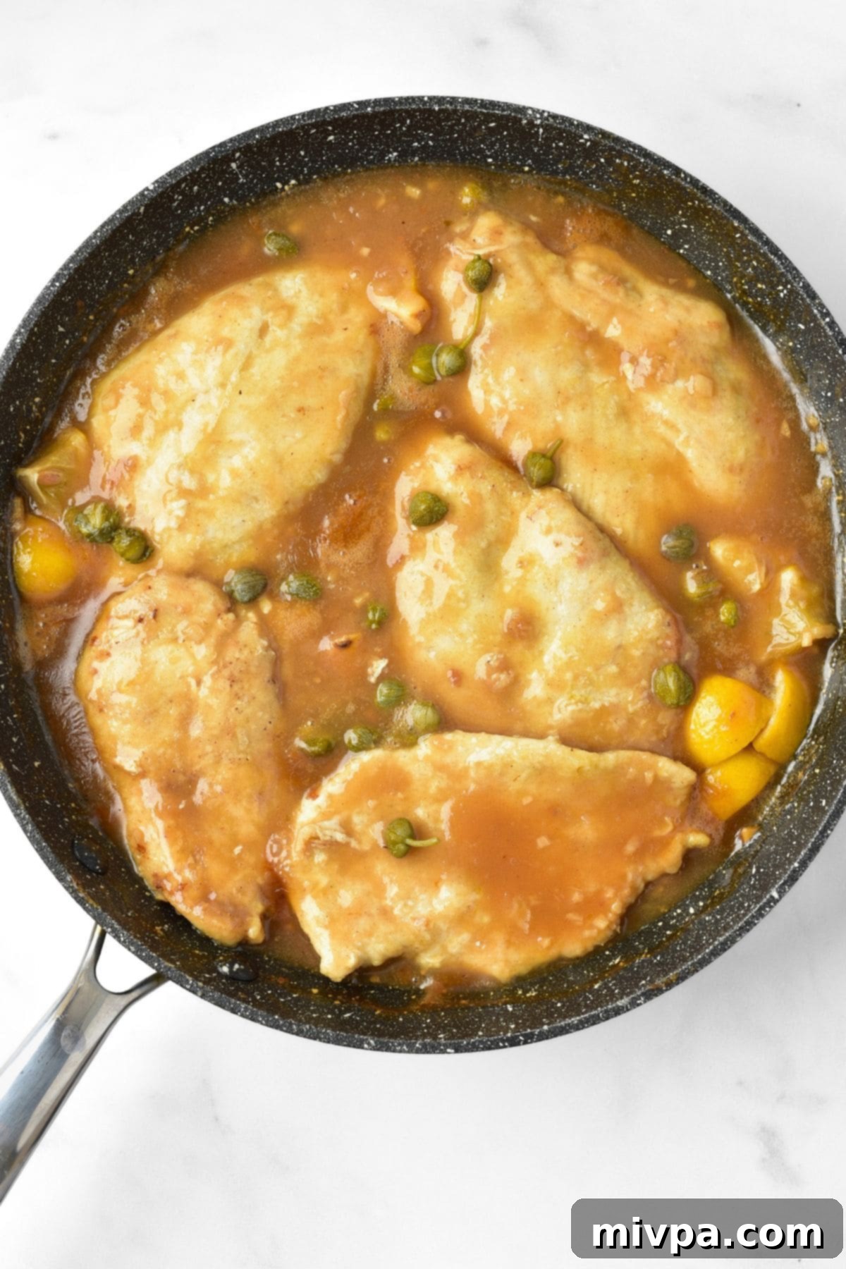 Top down view of slices of chicken in a sauce and topped with capers