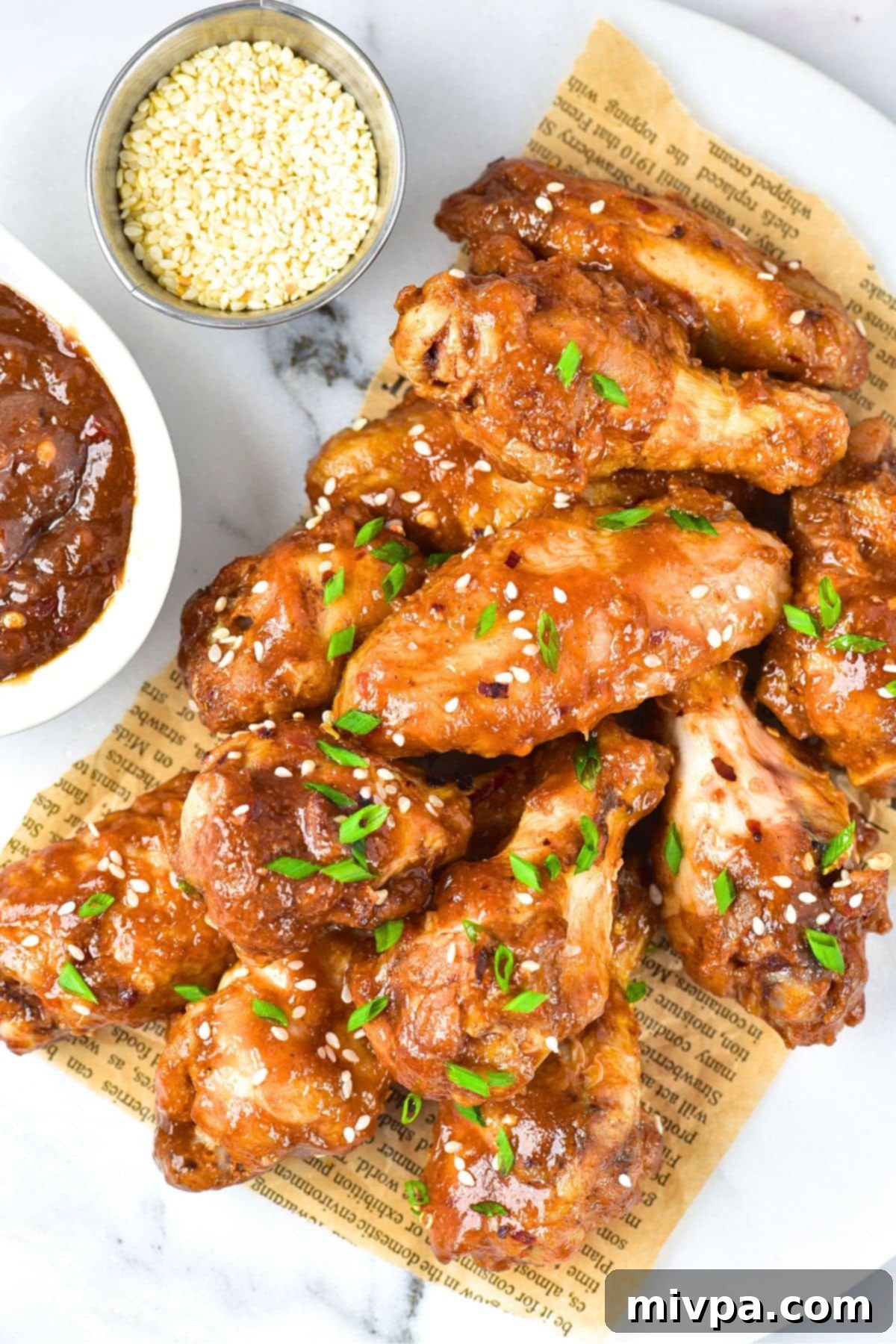 Top down view of sticky chicken wings on parchment paper, garnished with green onions and sesame seeds.