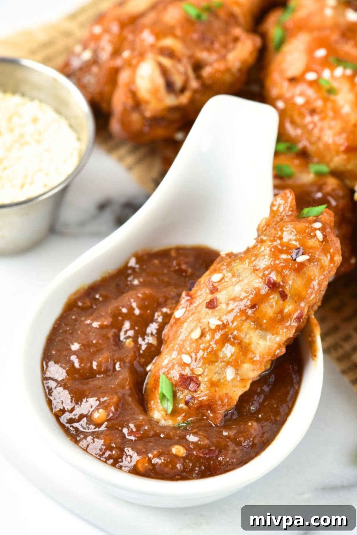 Dipping a baked chicken wing into a bowl of sweet and savory brown sauce.