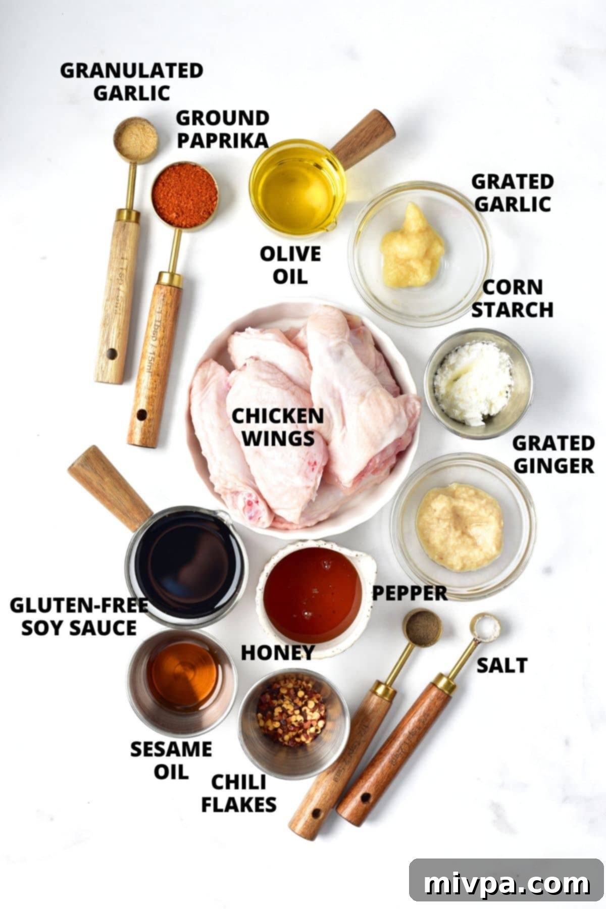Ingredients for sticky chicken wings recipe laid out on white board, including chicken wings, spices, honey, soy sauce, sesame oil, ginger, garlic, and chili flakes.