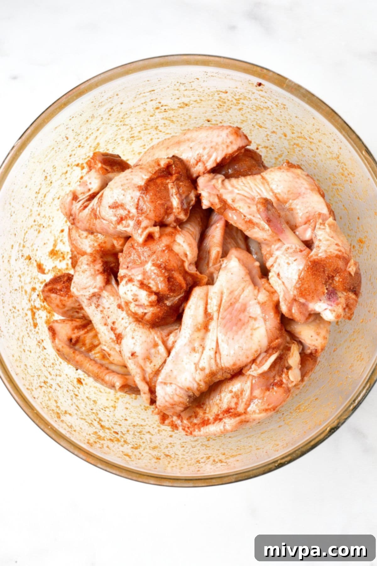 Marinating raw chicken wings in a glass bowl with spices.