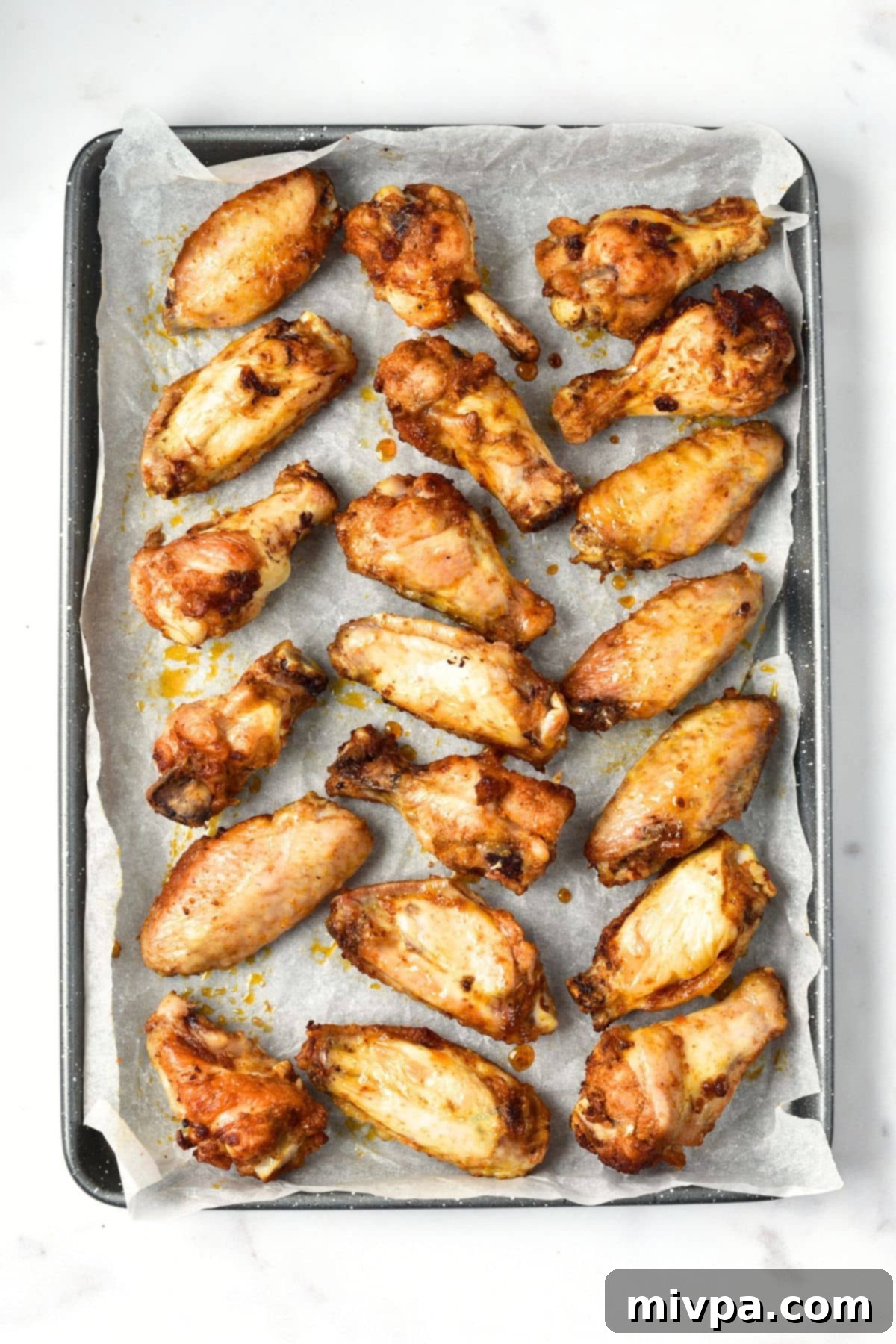 Baked chicken wings arranged on a parchment-lined baking sheet, ready for the glaze.
