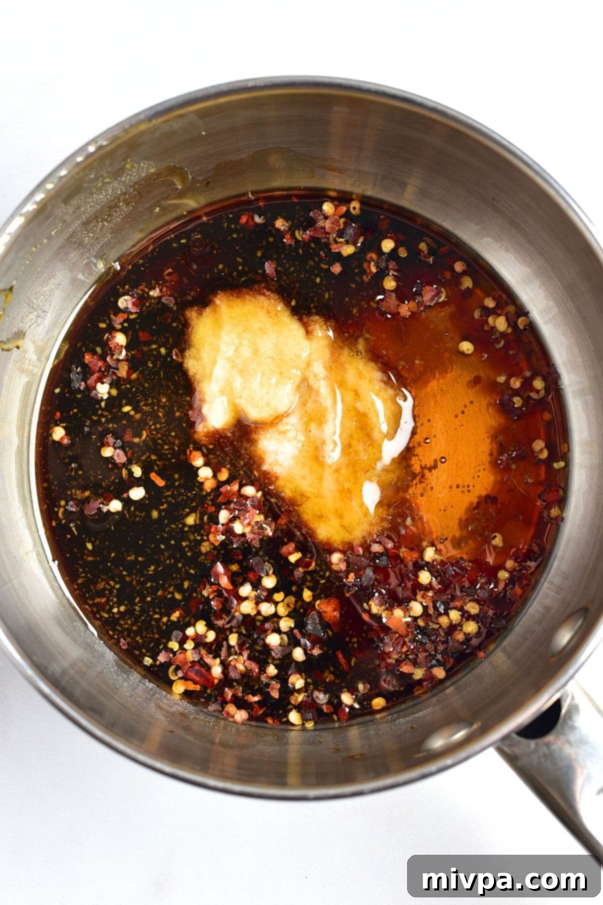Red pepper flakes, grated garlic, soy sauce, olive oil, and sesame oil in a small saucepan, ready to be cooked.