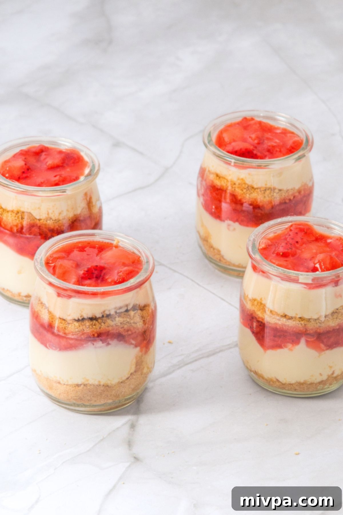 No Bake Gluten Free Strawberry Cheesecake Cups 2 Jars filled with graham cracker crumbs, cream cheese, and strawberry sauce.