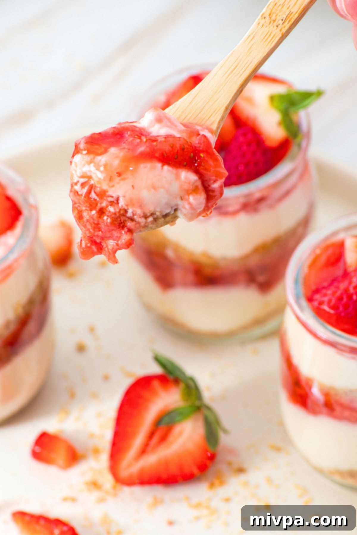 No-Bake Cheesecake Cups (Gluten-Free) Holding up spoonful of strawberry cheesecake.