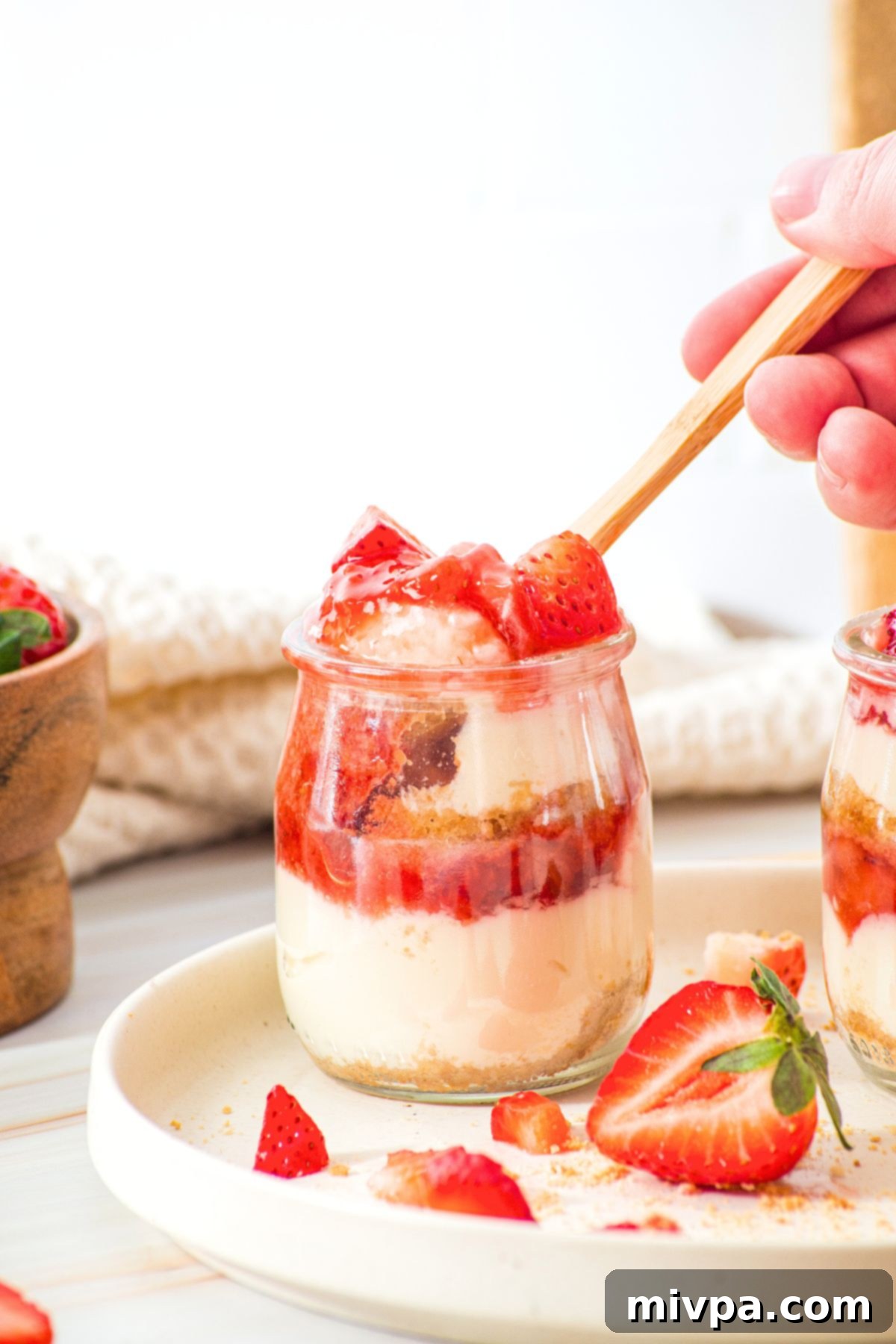 Strawberry Cheesecake Dessert Cups (Gluten-Free, No-Bake) Holding up a spoonful of strawberry dessert from jar.