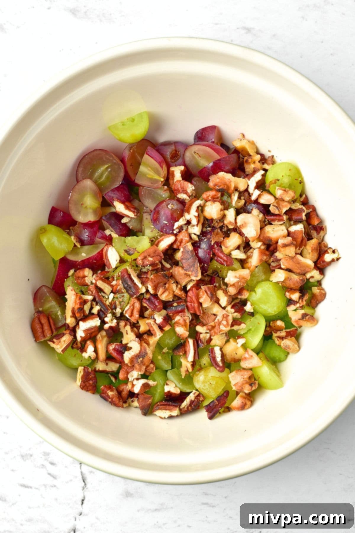 Waldorf Salad with Grapes Chopped nuts, sliced grapes and chopped celery in white bowl.
