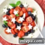 Stars and Stripes Caprese Salad 2 Cherry tomatoes, blueberries, mozzarella stars and basil leaves in bowl.