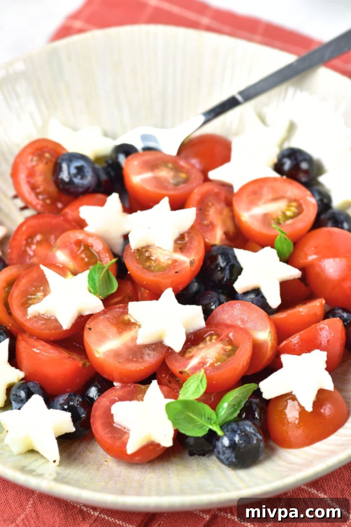 Patriotic Caprese Salad with Blueberries Up close view of star shaped mozzarella on top of cherry tomatoes and blueberries.