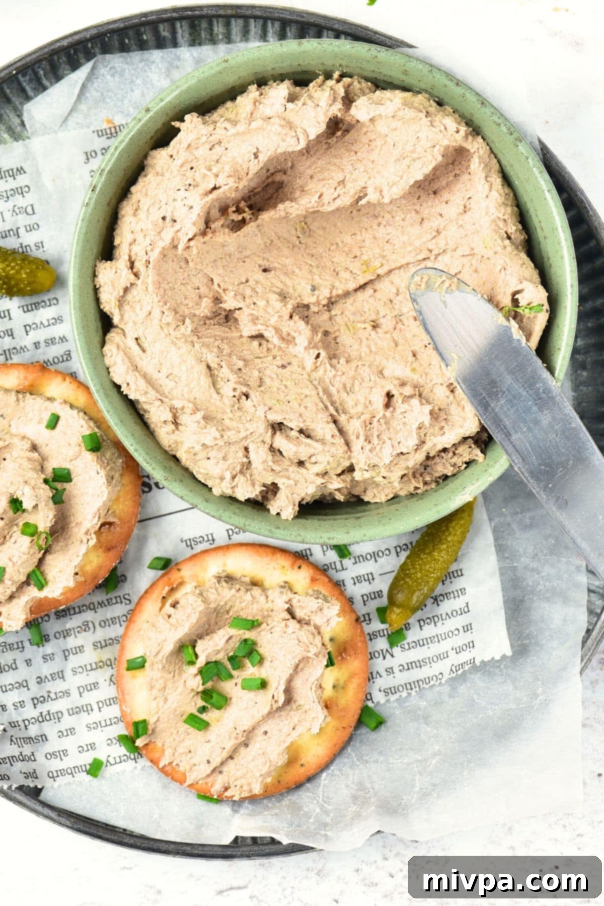 A rustic wooden board holds a bowl of homemade liver pate alongside an assortment of crisp crackers.