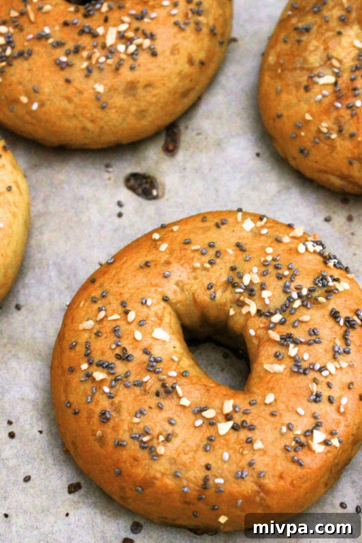 Gluten-Free Vegan Bagel Recipe (Chewy and Tender!) Up-close view of a single gluten-free everything bagel resting on parchment paper after baking, showing its perfect golden crust.