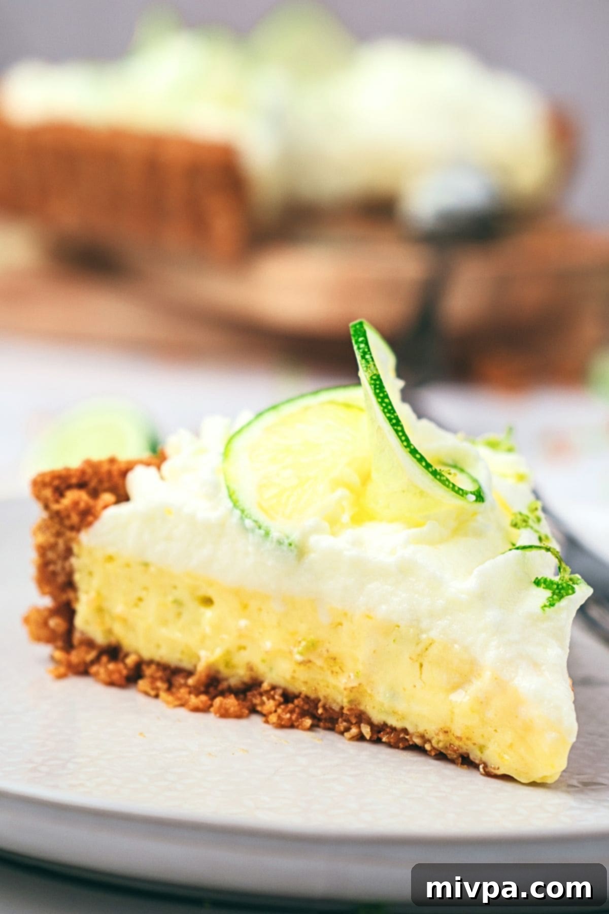 A perfectly sliced gluten-free key lime pie with a golden graham cracker crust and fluffy whipped cream on a white plate, ready to be enjoyed.