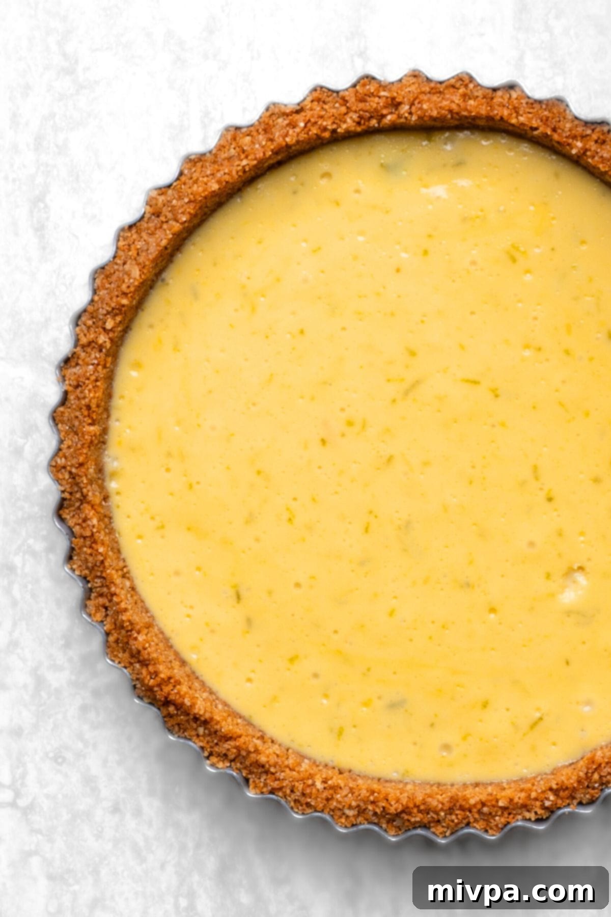 A freshly baked gluten-free key lime tart, with a firm, vibrant green filling, cooling in its pan.