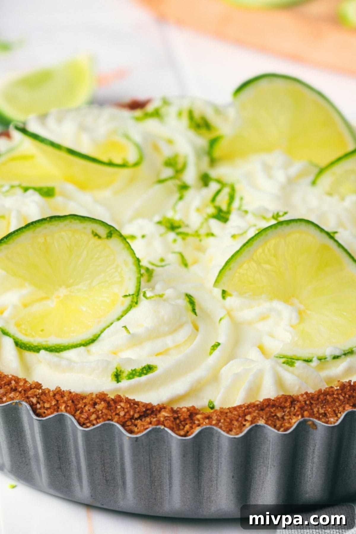 A whole gluten-free key lime pie, beautifully set in a metal pie pan, garnished with whipped cream and lime zest.