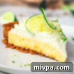 A pristine slice of key lime pie on a white plate, showcasing the creamy filling, golden crust, and whipped cream topping.