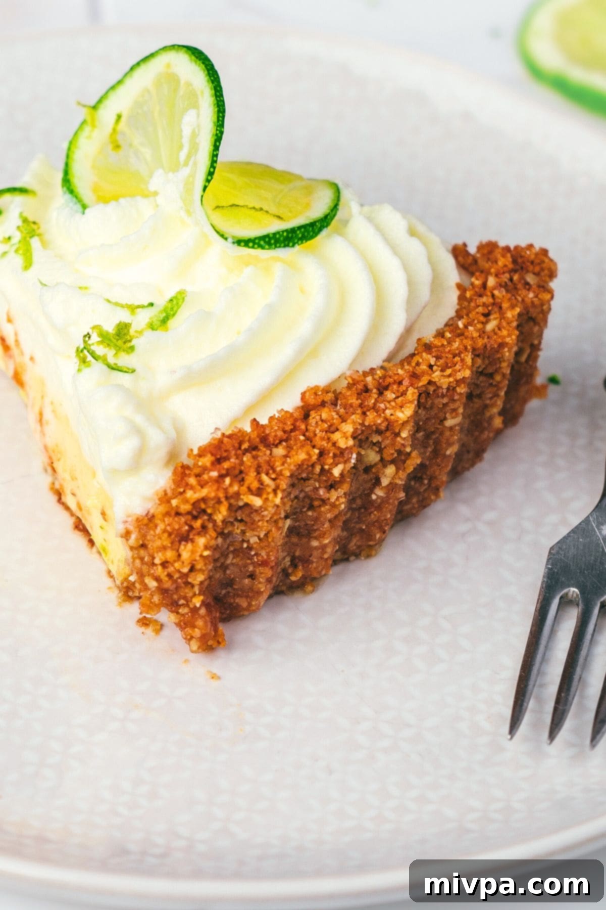 Close-up shot of a single slice of key lime pie, richly adorned with a swirl of whipped cream and a sprinkle of lime zest, highlighting its inviting texture.