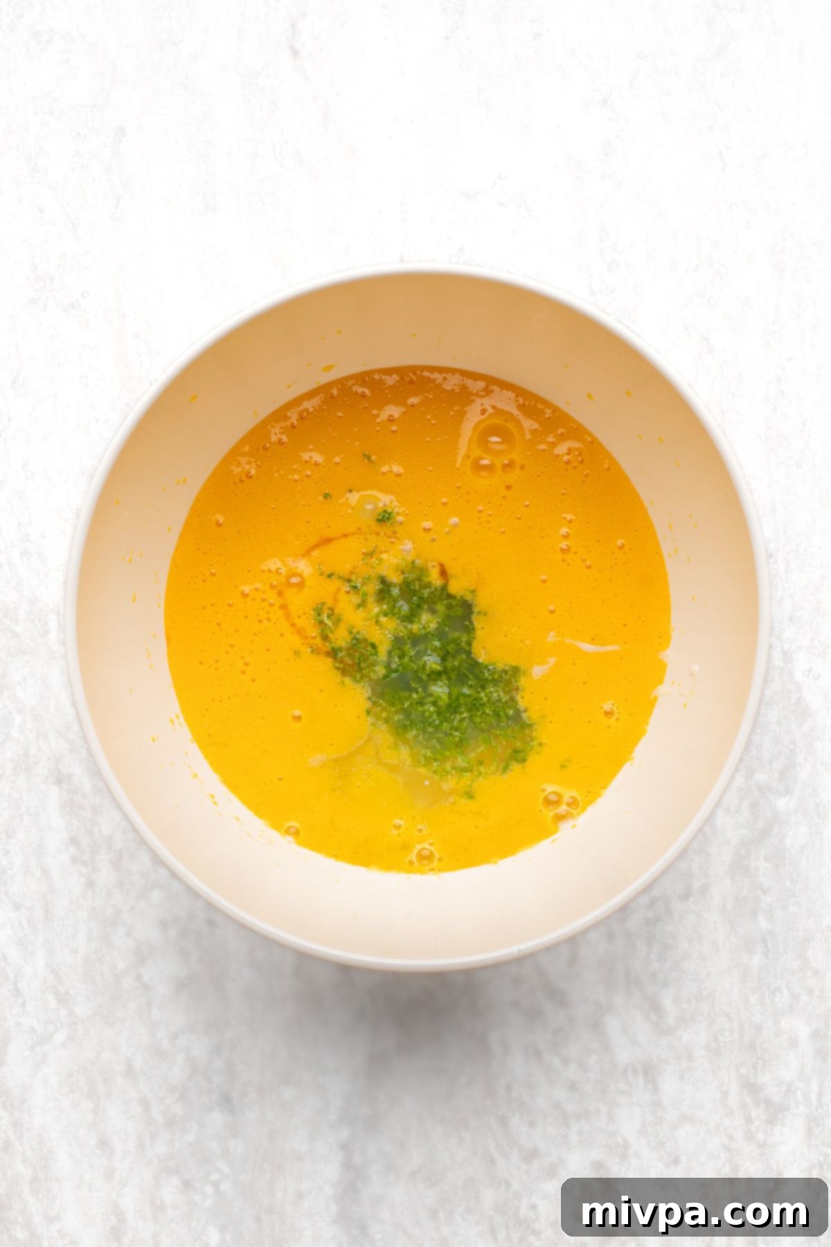 A bowl containing beaten egg yolks, vibrant key lime zest, and clear vanilla extract, ingredients for the GF Key Lime Pie filling.
