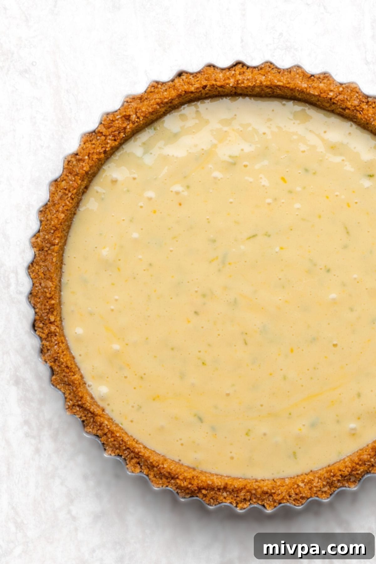 The smooth, uncooked key lime filling poured into the golden graham cracker pie crust, ready for baking.