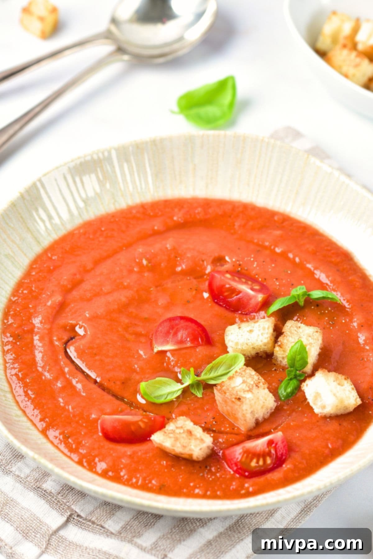 A bowl of crouton-topped gazpacho, garnished with fresh basil.