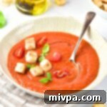 A bowl of gazpacho soup topped with basil leaves and crunchy croutons