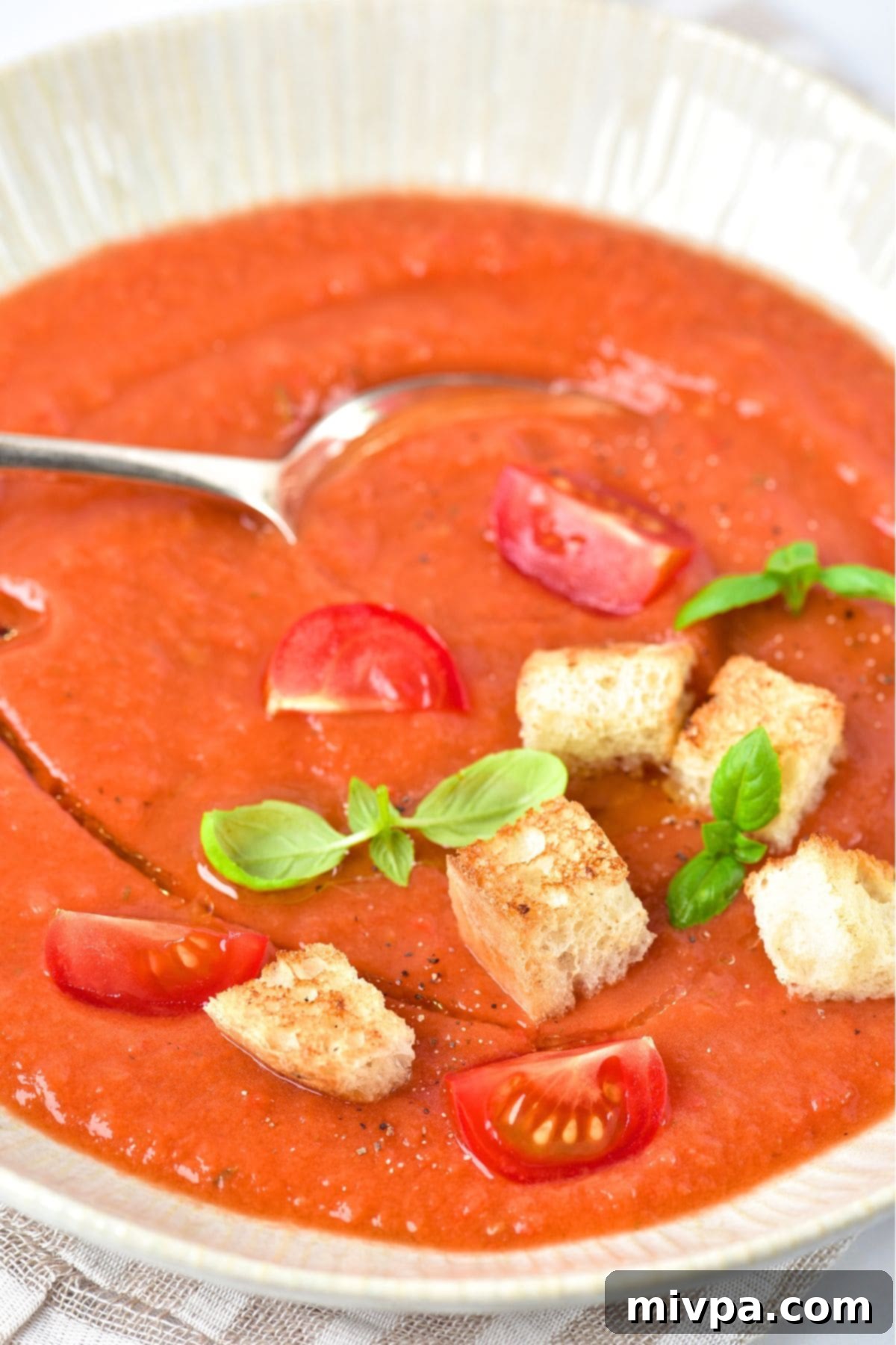 A bowl of gluten-free gazpacho soup topped with crunchy croutons and a sprig of basil.