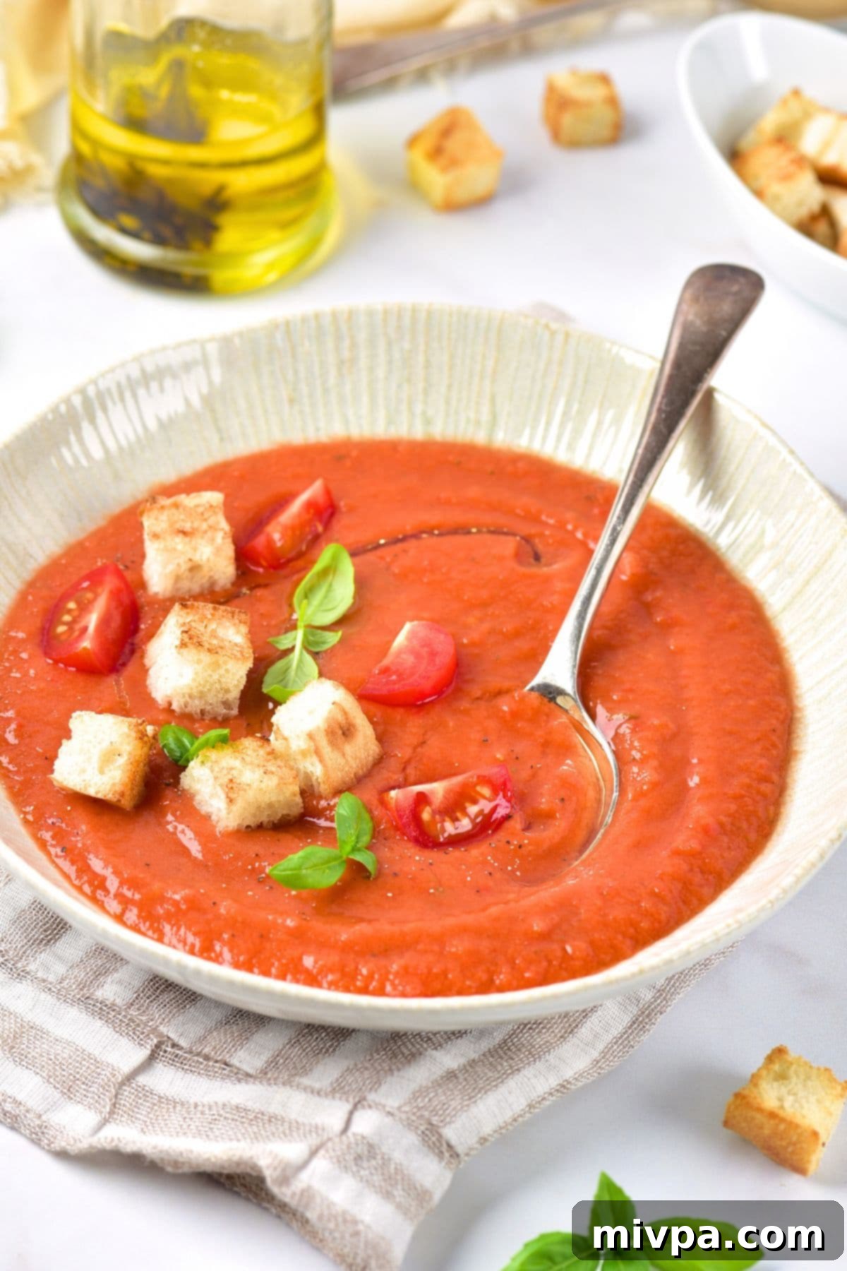A spoon dipping into a bowl of perfectly chilled gazpacho, garnished with fresh herbs and diced vegetables.