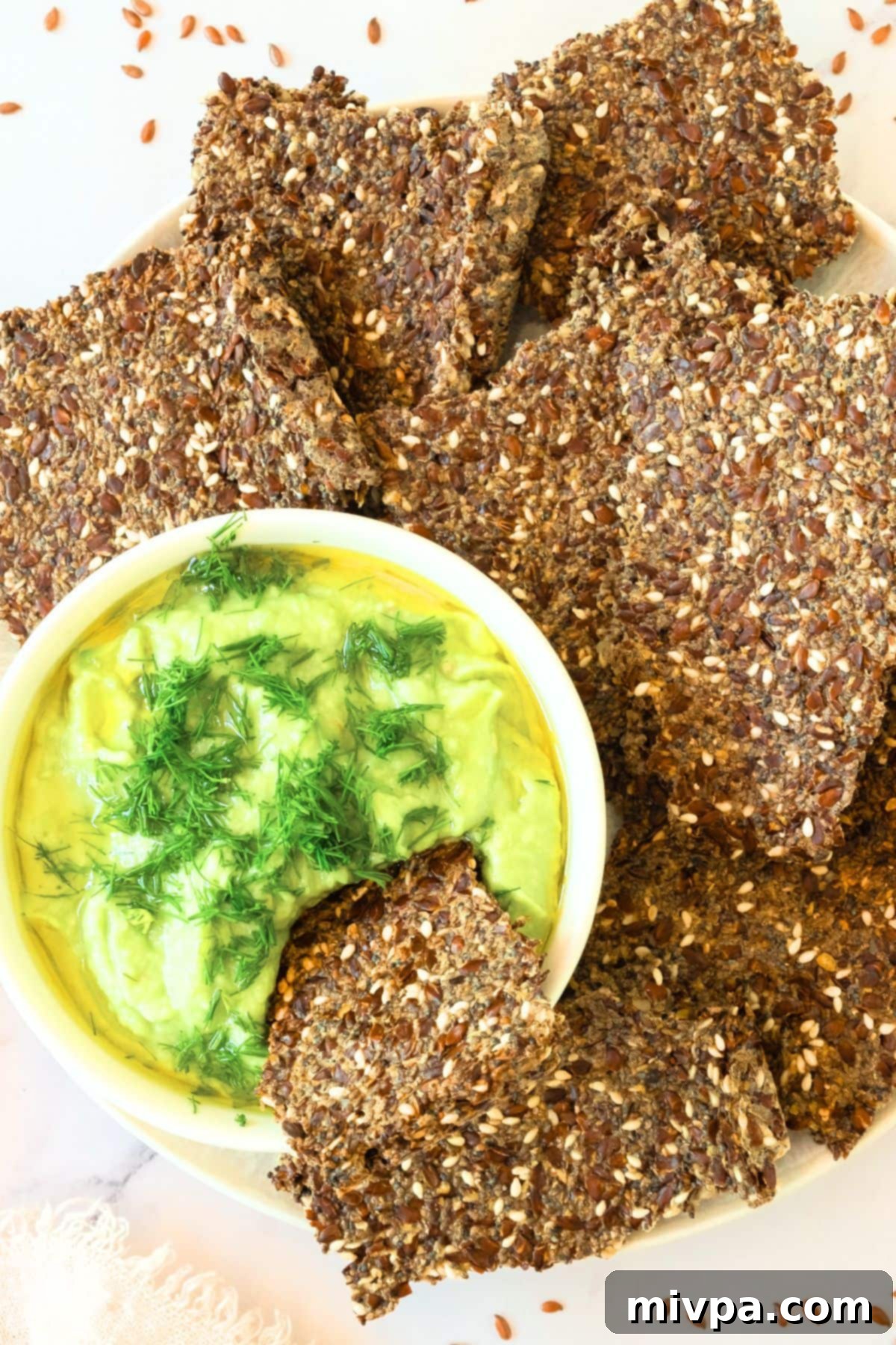 Flaxseed Crackers (Gluten-Free, Vegan) with Guacamole A plate of golden flaxseed crackers served with a vibrant bowl of guacamole dip, showcasing their crispy texture.